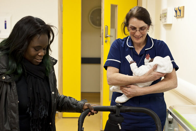 Mum getting the pram ready while a nurse holds her baby