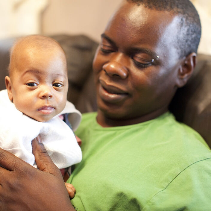 Dad sat on the sofa holding his baby looking at him lovingly