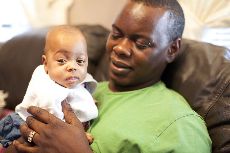Dad sat on the sofa holding his baby looking at him lovingly