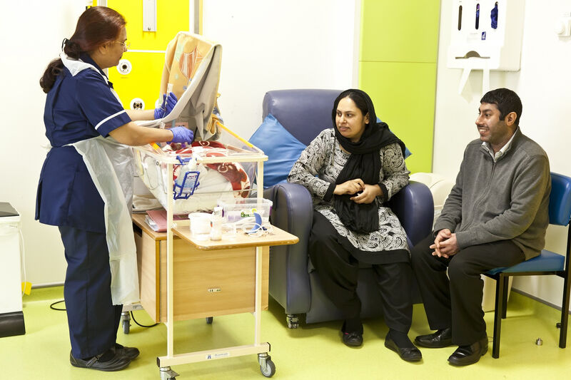 Nurse tube feeding a baby in a cot while the parents sit nearby