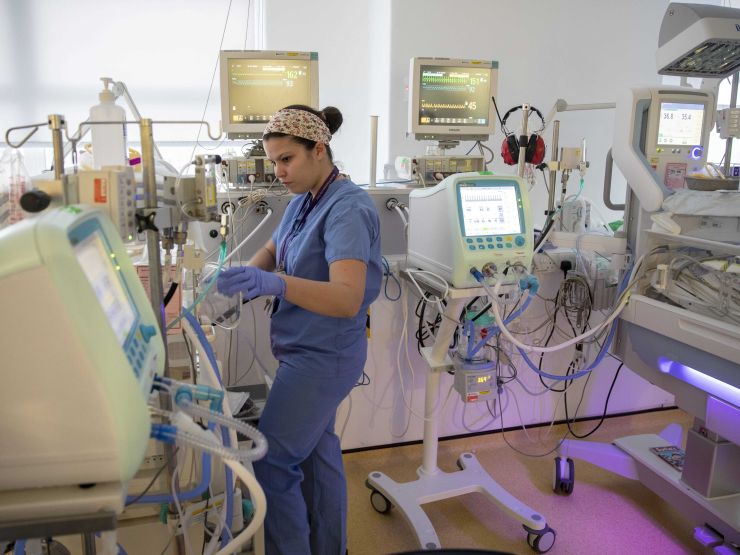 Neonatal nurse stands next to incubator look at the instrument readings