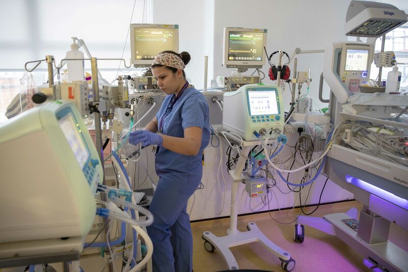 Neonatal nurse stands next to incubator look at the instrument readings