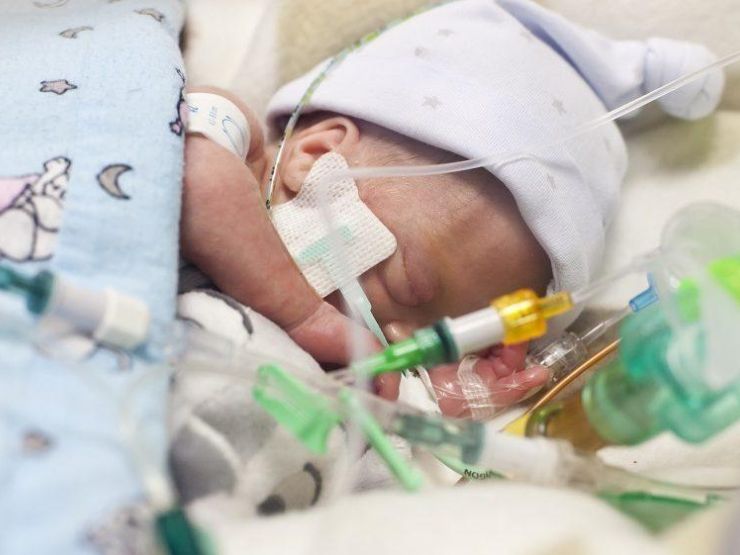 Premature baby wearing a wooly hat sleeping peacefully attached to several tubes