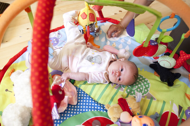 Baby in pyjamas lying on their back looking at elevated toys.