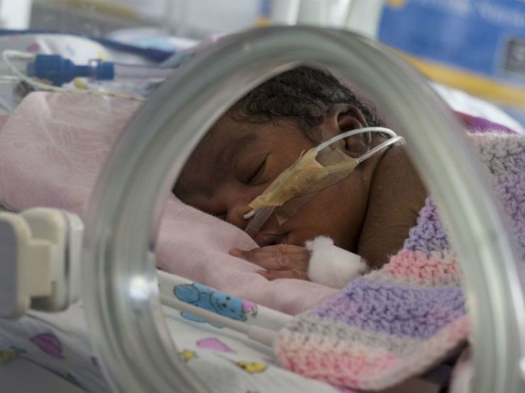 Baby covered in blanket attached to feeding tube sleeping peacefully in an incubator