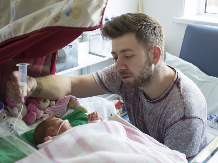 Dad sat by his baby holding a syringe of milk in the air slowly tube feeding his baby