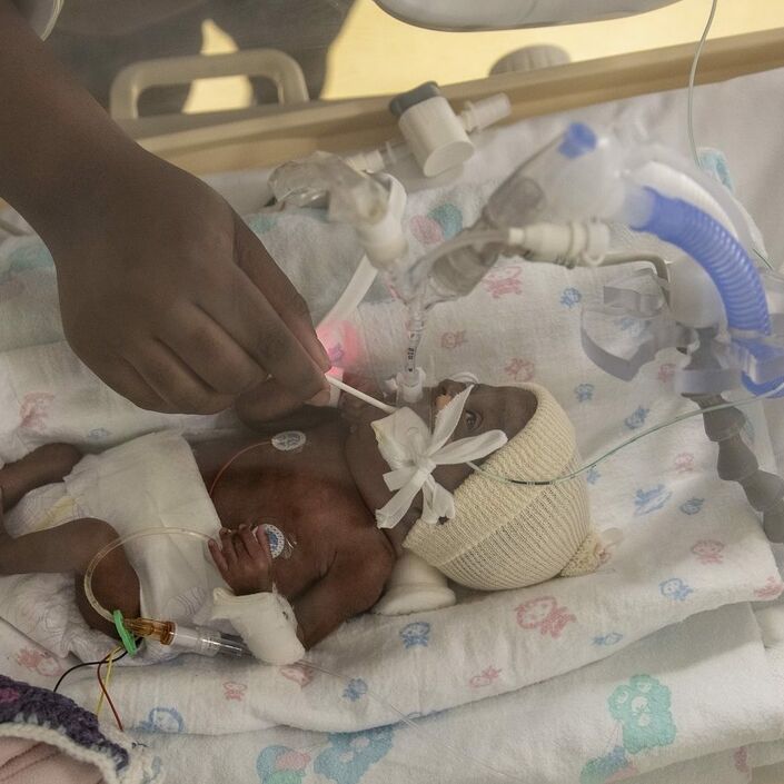 Baby in incubator with mum cleaning mouth with a cotton wool bud