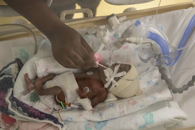 Baby in incubator with mum cleaning mouth with a cotton wool bud