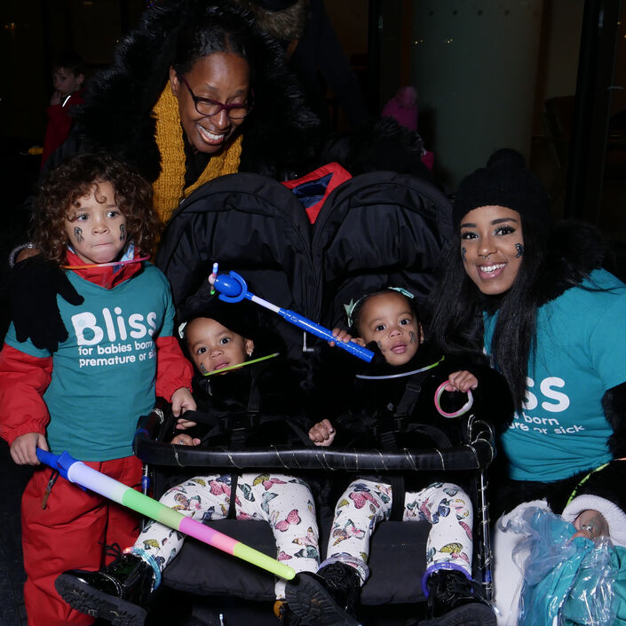 2 Adults, young child and 2 toddlers in a twin buggy wrapped up warm in darkness