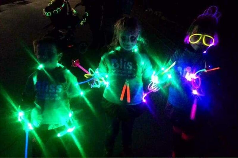 Darkness with 3 people wearing Bliss t-shirts lit up with glow sticks and lights