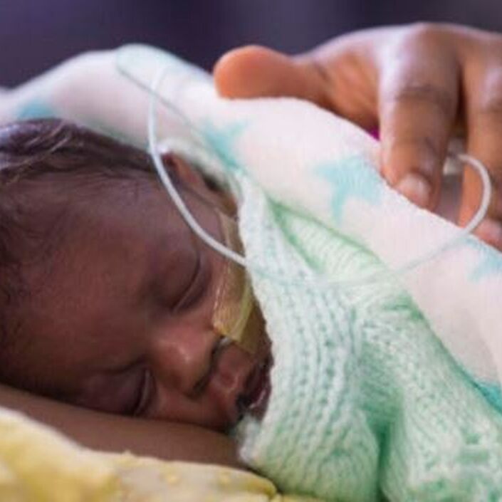 Baby wrapped in blanket sleeping on mother's chest with her hand on the baby's back