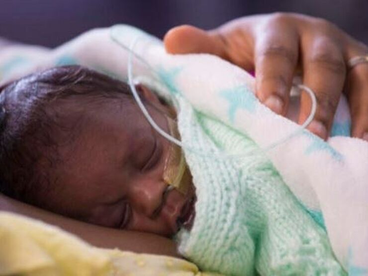 Baby wrapped in blanket sleeping on mother's chest with her hand on the baby's back