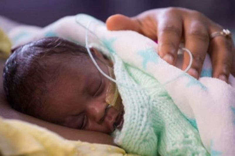 Baby wrapped in blanket sleeping on mother's chest with her hand on the baby's back