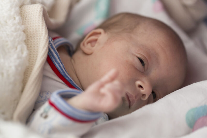 Baby lying in a cot covered in a wool blanket