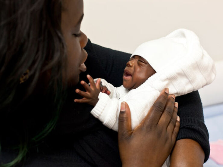 Mother holding and looking down at her baby who is reaching up towards her face.