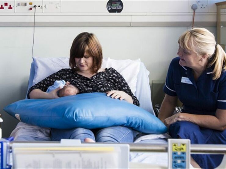 Mother sitting on a hospital bed breastfeeding her baby with a nurse nearby