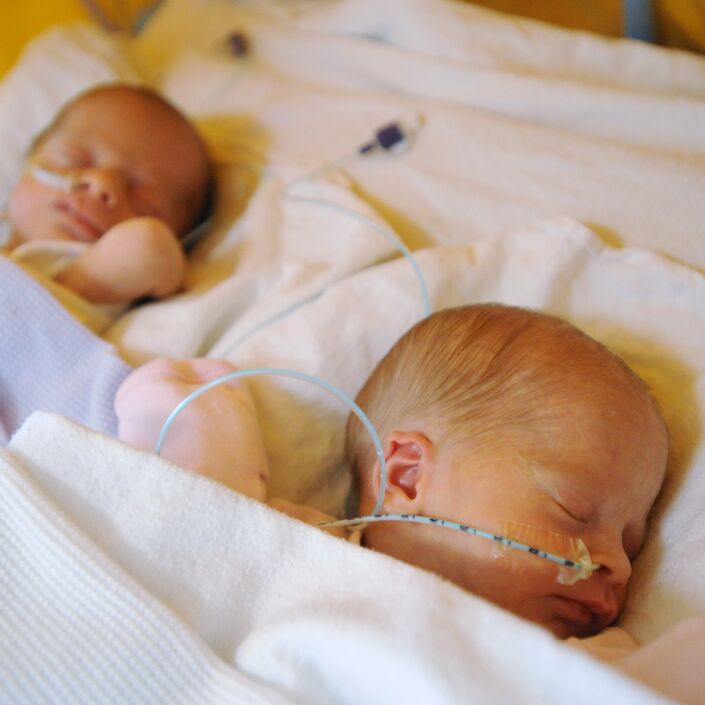 Two babies laying side by side wrapped in blankets and sleeping, with tubes attached to their nose