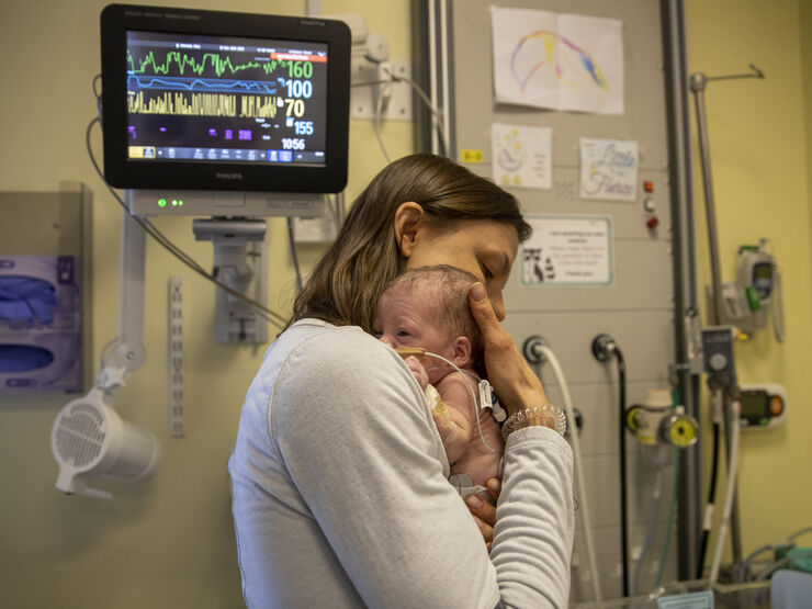 Mum embracing her baby tightly in her chest with an incubator machine behind them