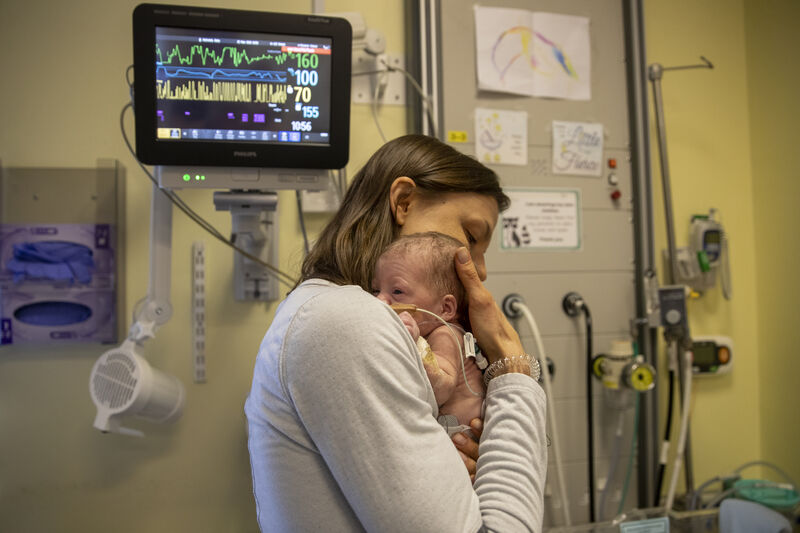 Mum embracing her baby tightly in her chest with an incubator machine behind them