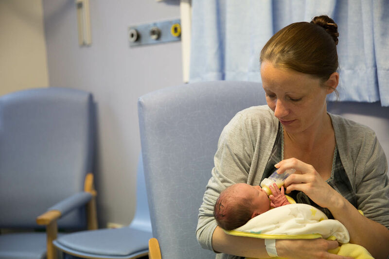 Mum in hospital, bottle feeding her baby who is wrapped in a blanket