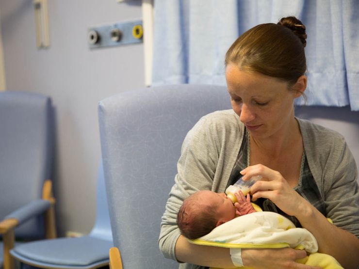 Mum in hospital, bottle feeding her baby who is wrapped in a blanket