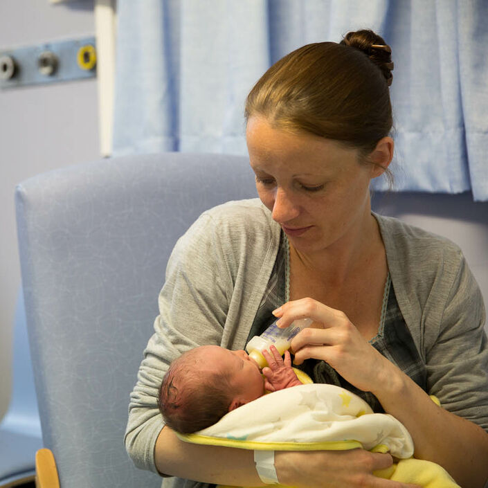 Mum in hospital, bottle feeding her baby who is wrapped in a blanket