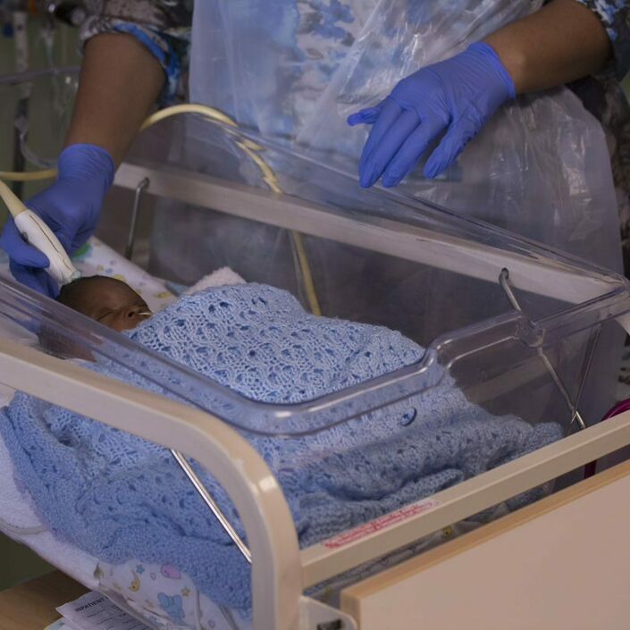 Healthcare professional with gloves on touching a baby's head with a small medical device