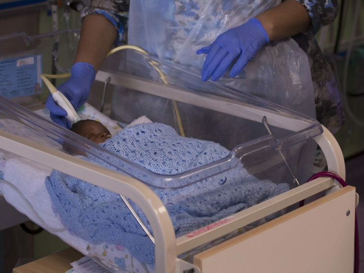 Healthcare professional with gloves on touching a baby's head with a small medical device