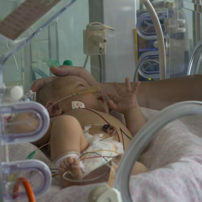 Baby in an incubator with their parent gently cupping the top of their head