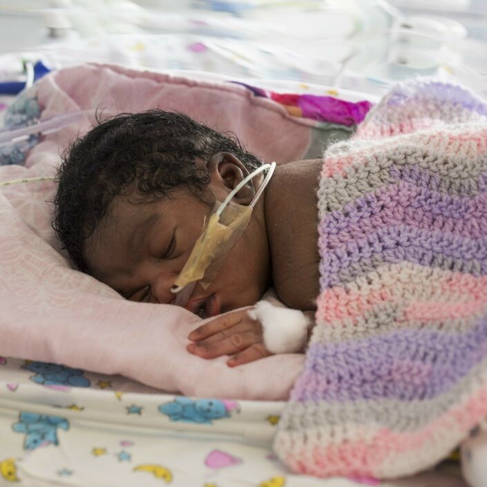 Baby covered in knitted blanket attached to feeding tubes sleeping in hospital bed