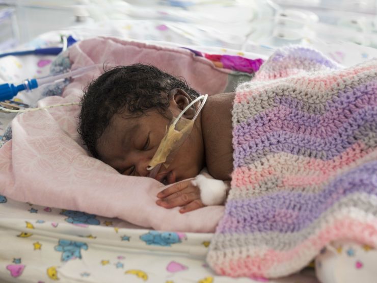 Baby covered in knitted blanket attached to feeding tubes sleeping in hospital bed