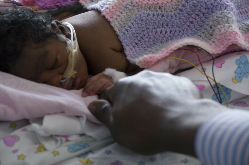Baby with tubes in nose covered in a blanket holding their father's finger