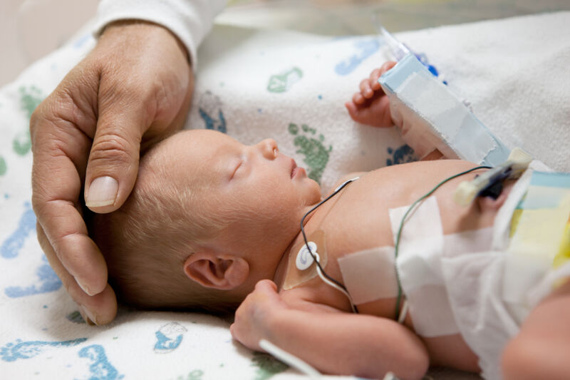 Father touching head of a premature baby in an incubator