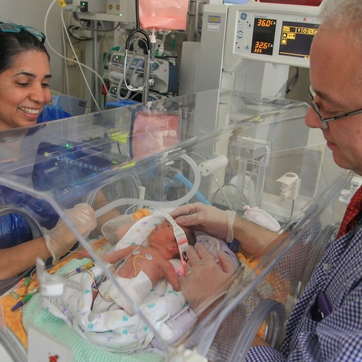 Doctor with his hands through an incubator looking after a baby while a nurse looks on smiling