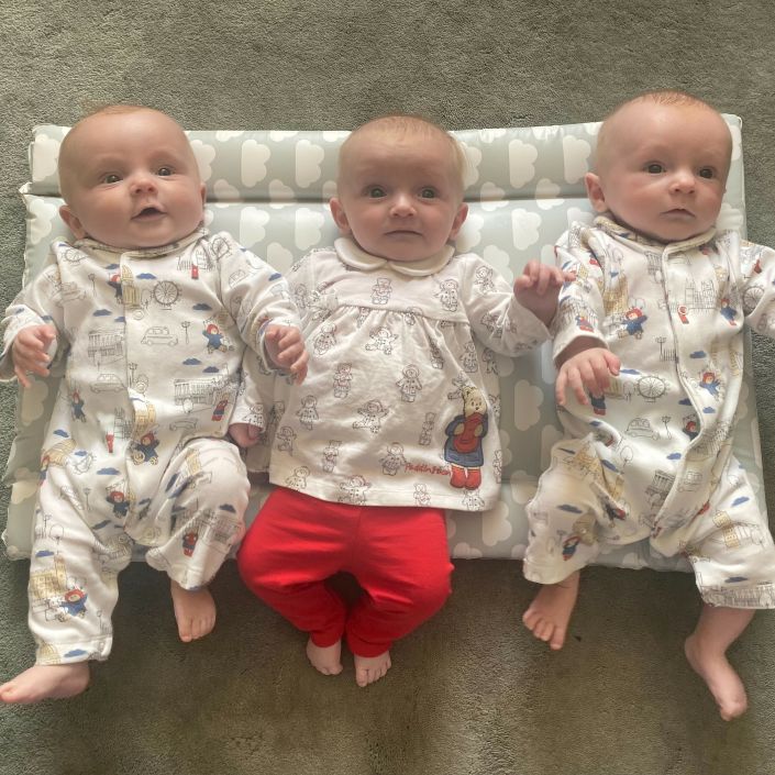 Three triplet babies lying next to each other on a cushion.
