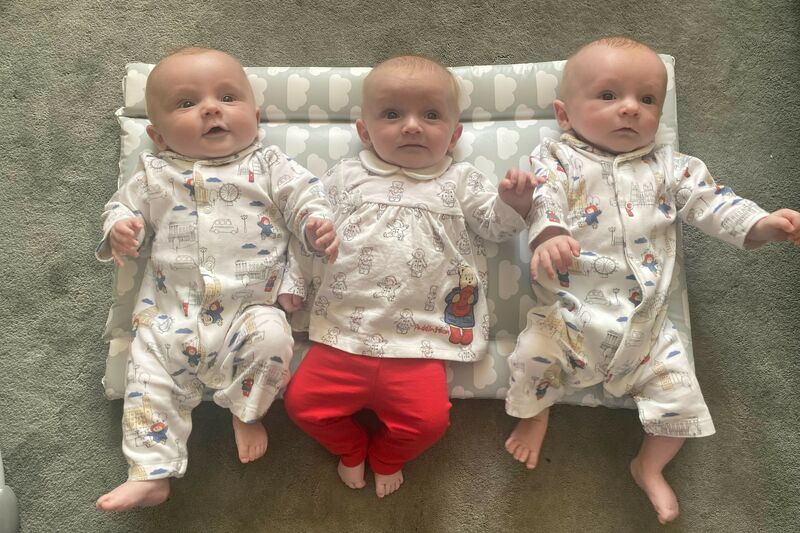 Three triplet babies lying next to each other on a cushion.