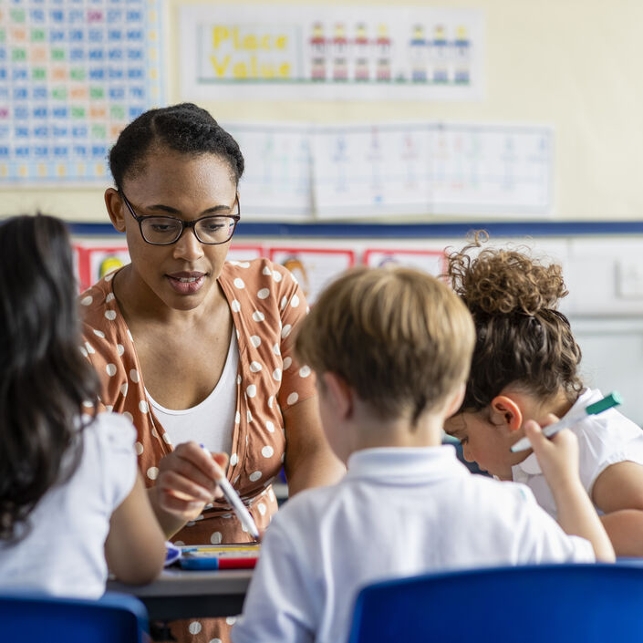 A teacher helping three primary school children with their work in a classroom