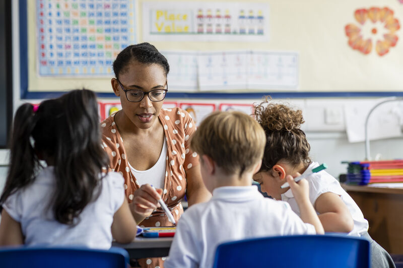 A teacher helping three primary school children with their work in a classroom