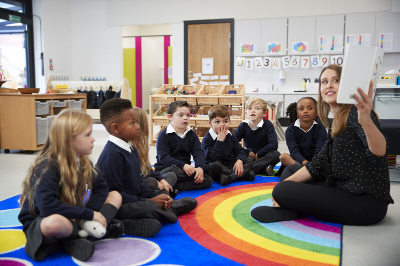 Primary school class sitting on the floor while teacher reads them a book