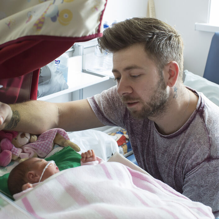 Dad looking over his sleeping baby while holding a syringe of milk above the baby to allow tube feeding