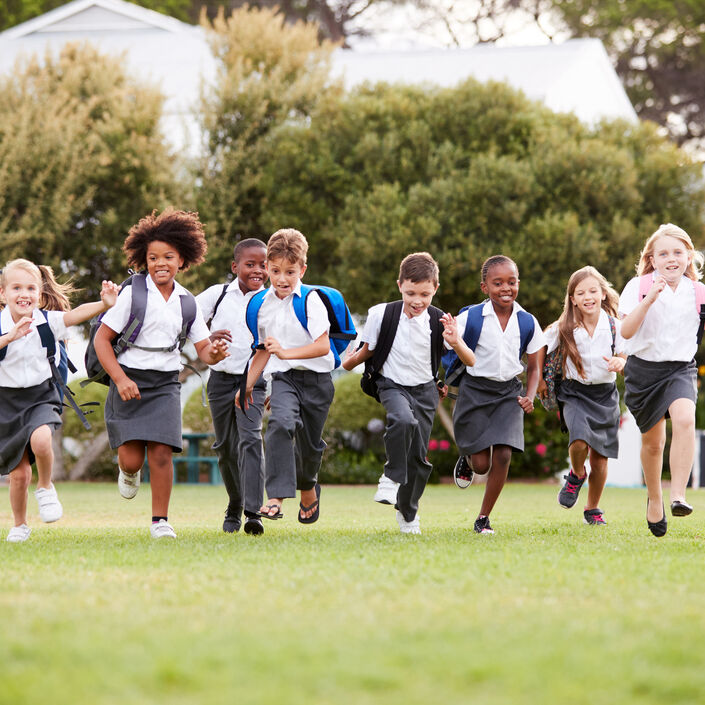 A group of primary school children running on grass with trees in background