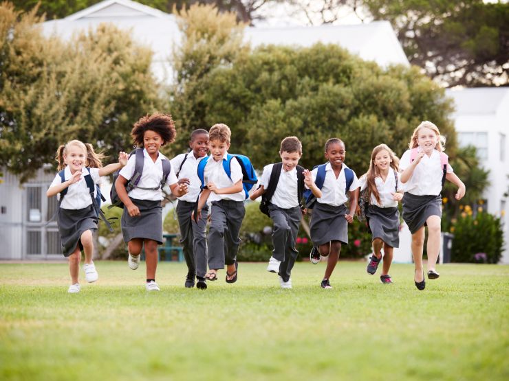 A group of primary school children running on grass with trees in background