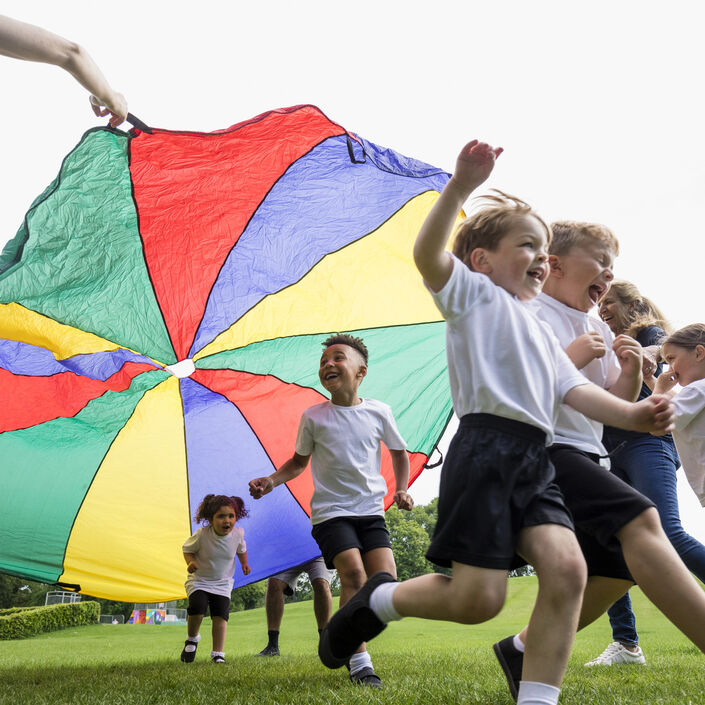 A group or children playing outside with a colourful parachute