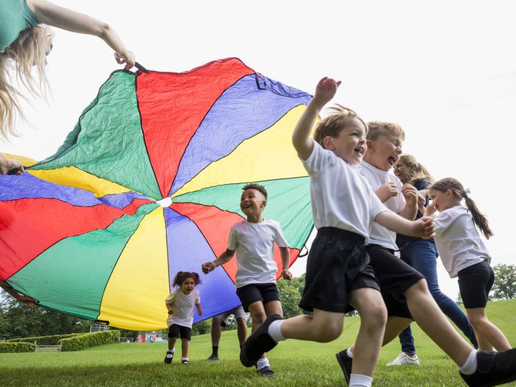 A group or children playing outside with a colourful parachute