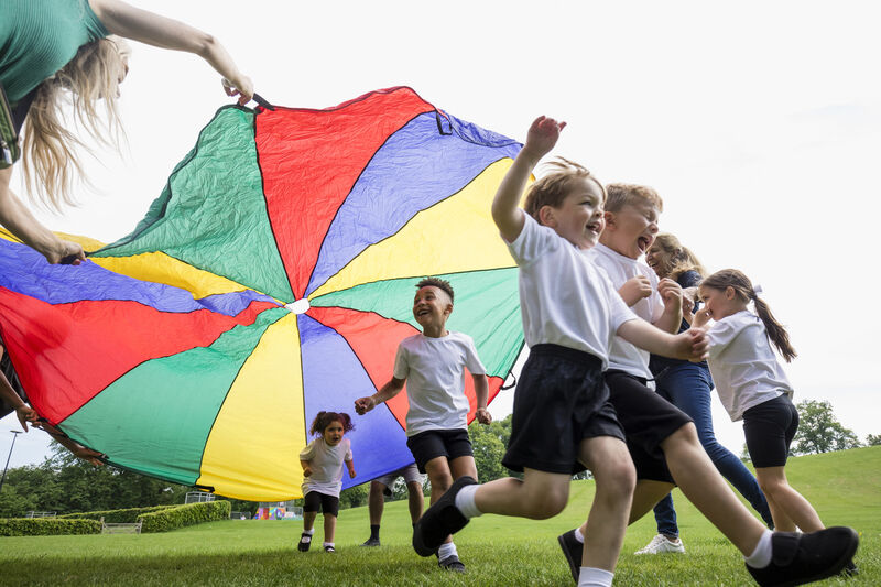 A group or children playing outside with a colourful parachute