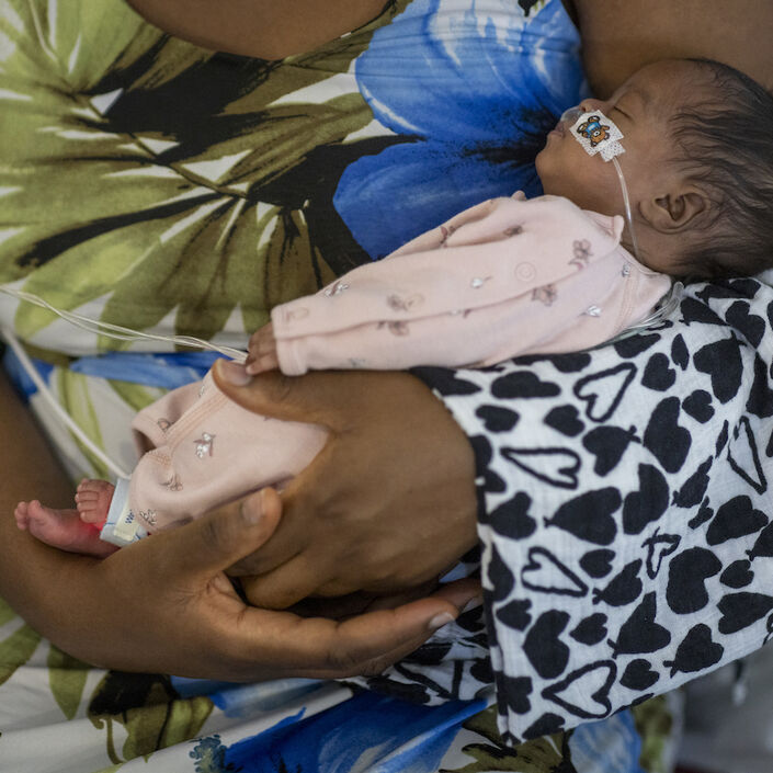 Mum holds baby wearing pyjamas and attached to feeding tube in her arms