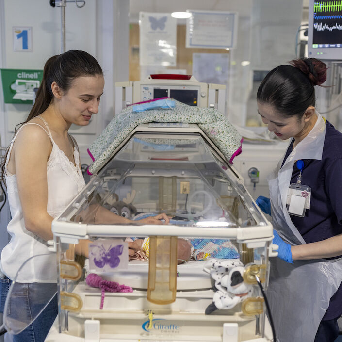 Mum and nurse standing over incubator looking in at premature baby