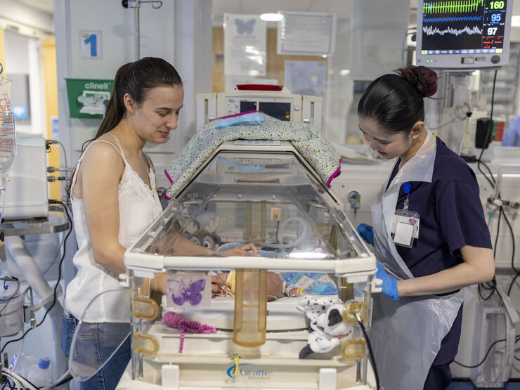 Mum and nurse standing over incubator looking in at premature baby