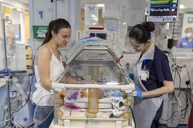 Mum and nurse standing over incubator looking in at premature baby