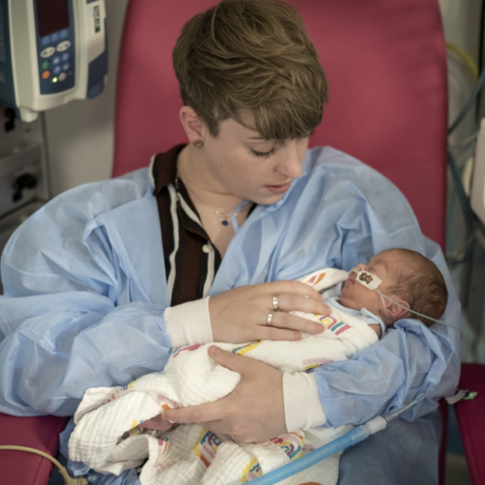Woman sat in a hospital chair holding her baby in her arms while looking down tenderly
